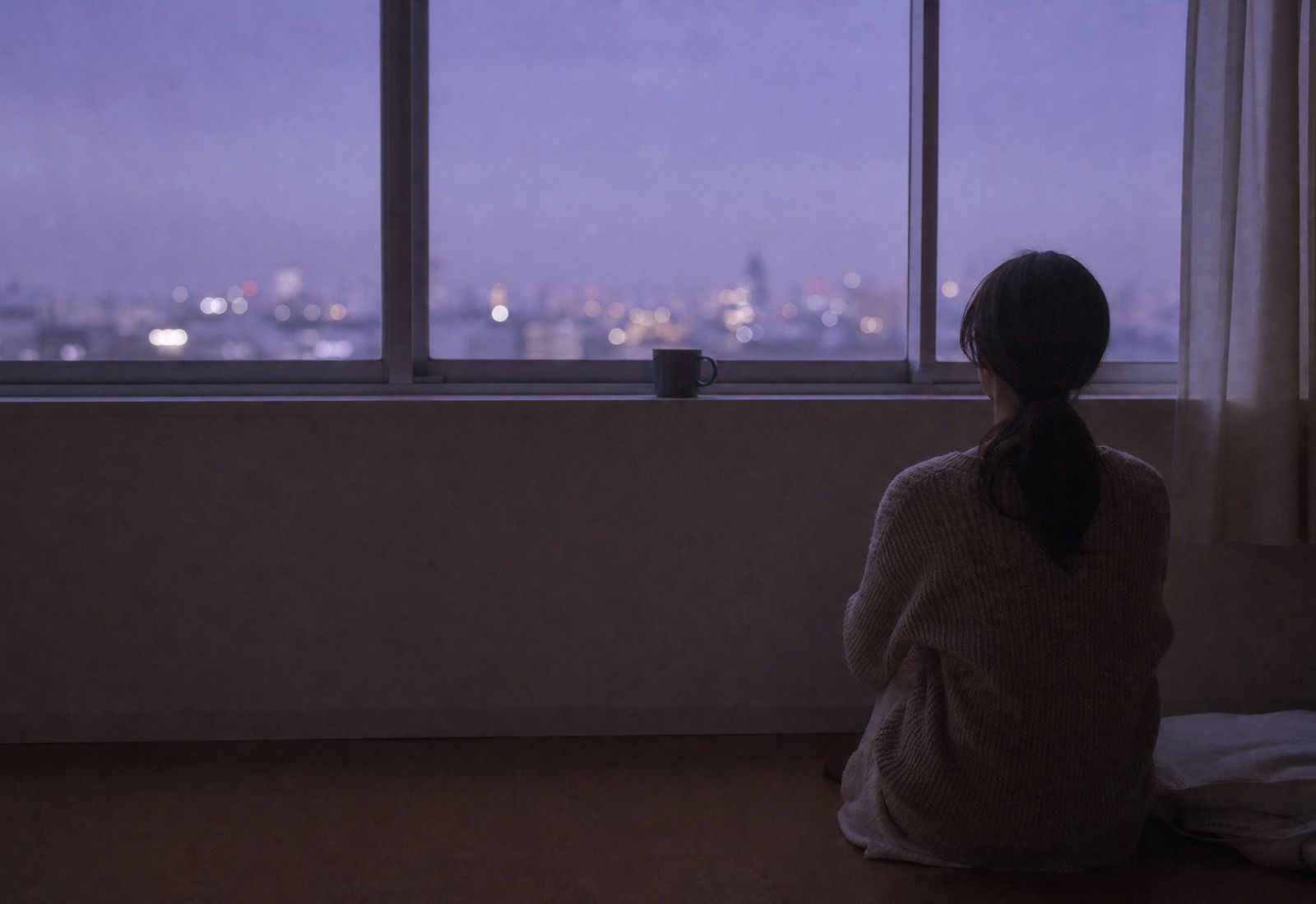 窓辺から夜の街を見る女性