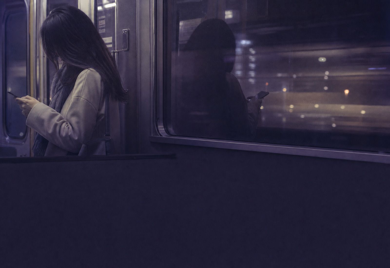 夜の電車でスマートフォンを見る女性