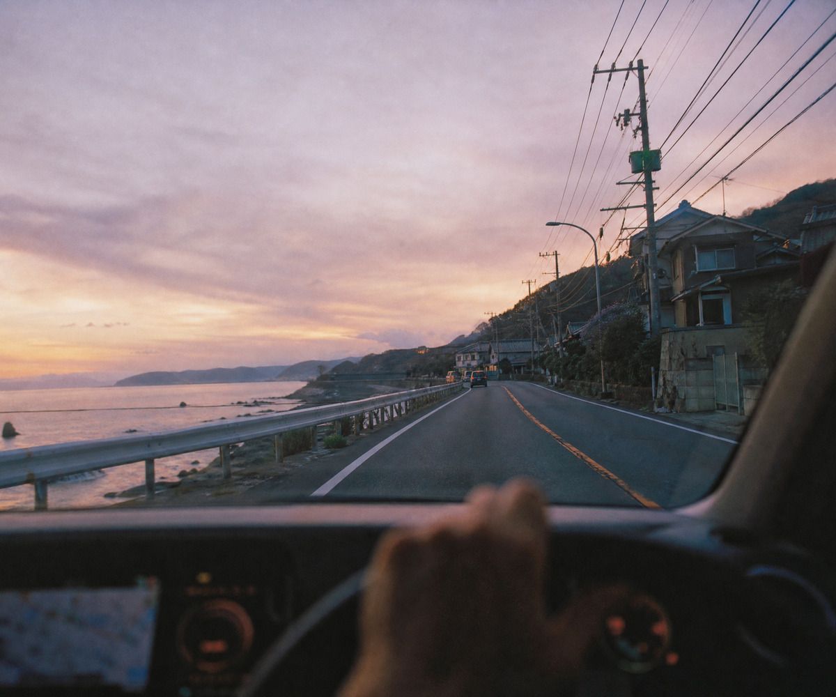 夕暮れの海沿いの道を走る車内